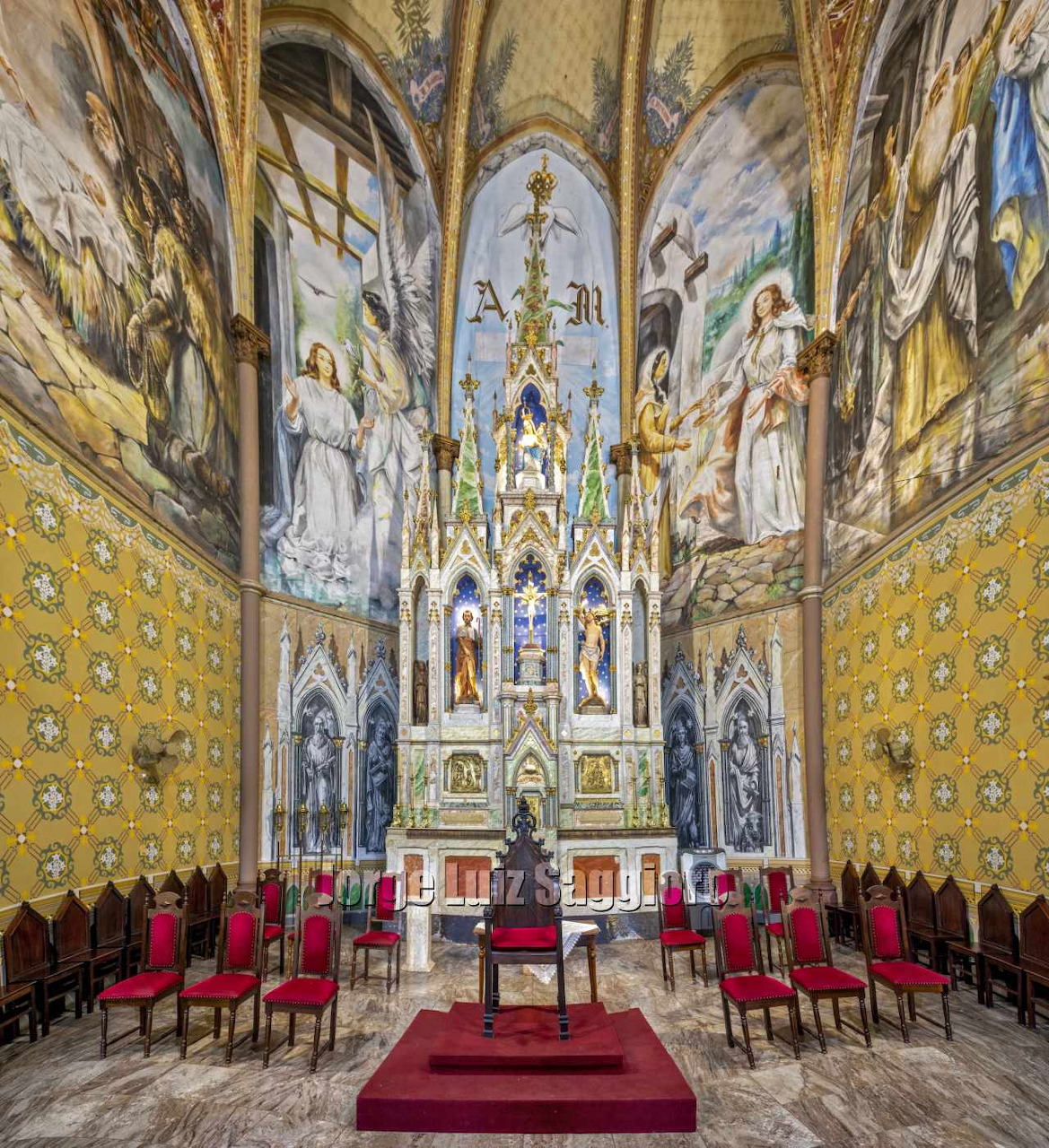 Ornate church interior with golden walls, baroque altar, red carpet, and rows of chairs in symmetrical layout