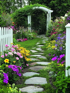 Stepping stone garden path lined with colorful flowers leading to white wooden arbor