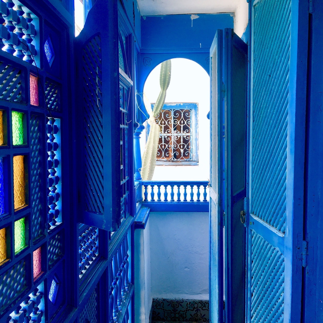 Narrow blue hallway with stained glass panels, ornate doors, and arched white walls in Tunisian architecture