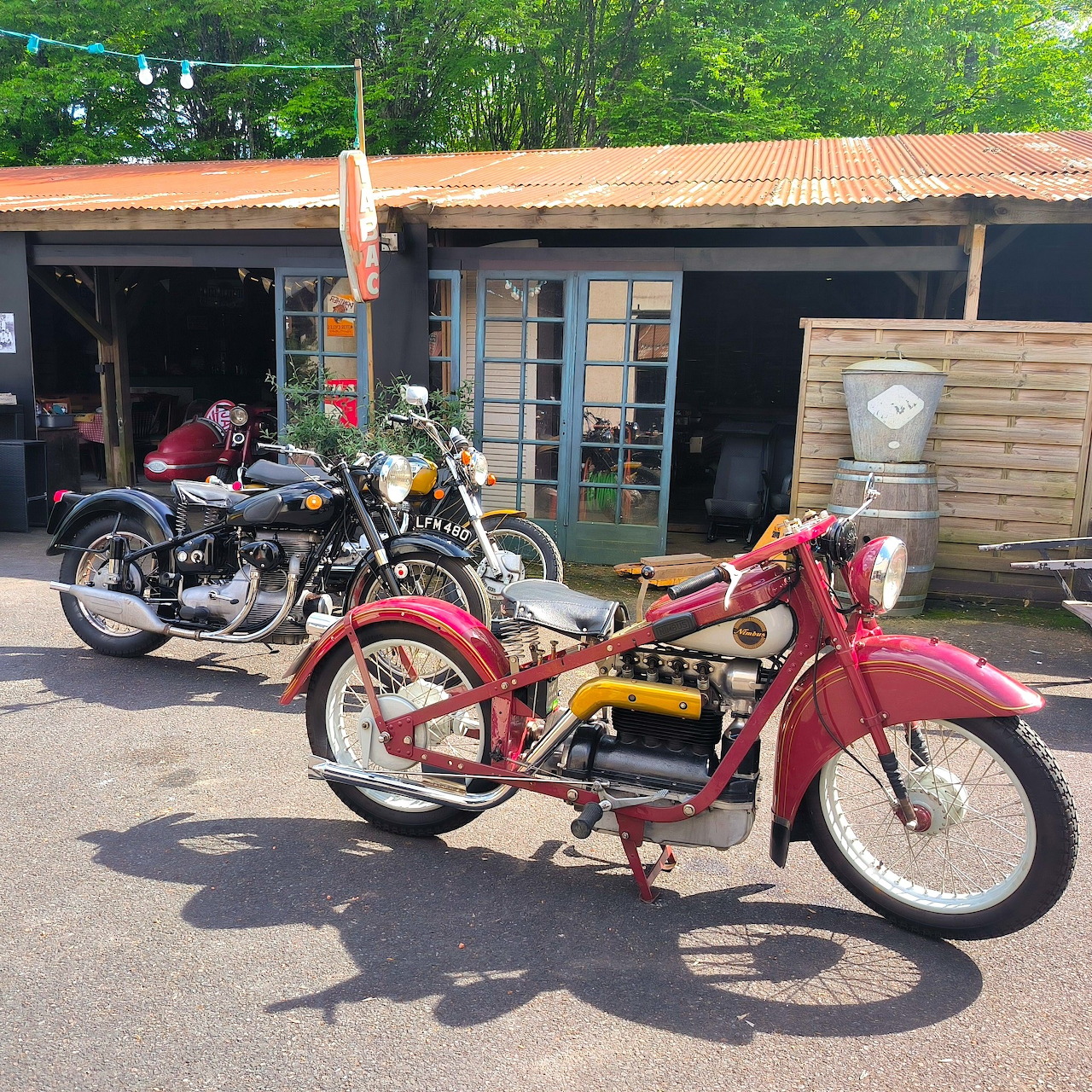 Red vintage Nimbus motorcycle and black Sunbeam bike parked outdoors in front of wooden garage