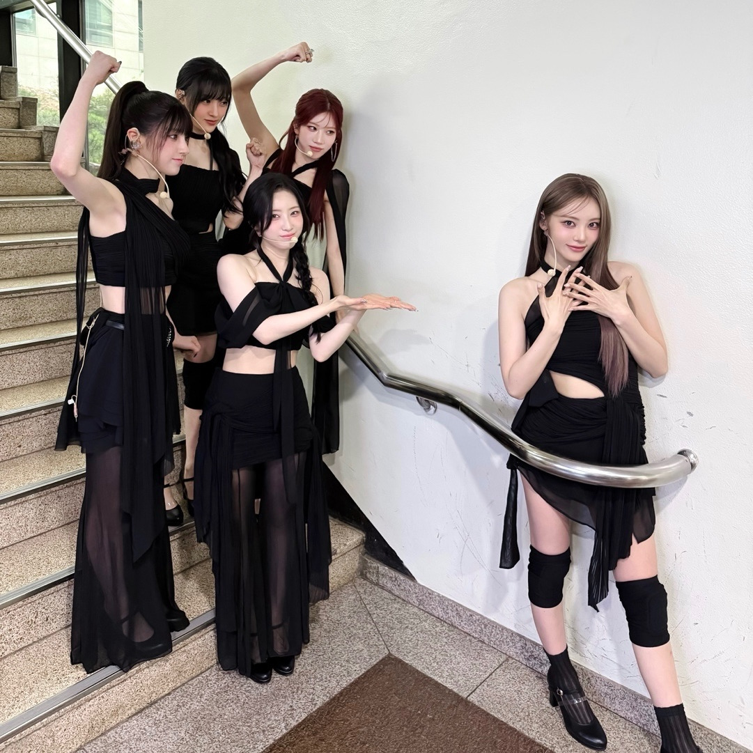 Five women in black outfits posing playfully on white staircase with metal railing
