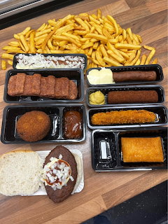 Fast food meal with fries, fried items, sauces, and sides in black containers on wooden surface