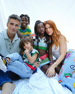 Family of five posing together on a light background, parents with three children in colorful outfits
