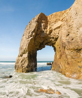 Natural stone arch on beach with ocean waves and blue sky