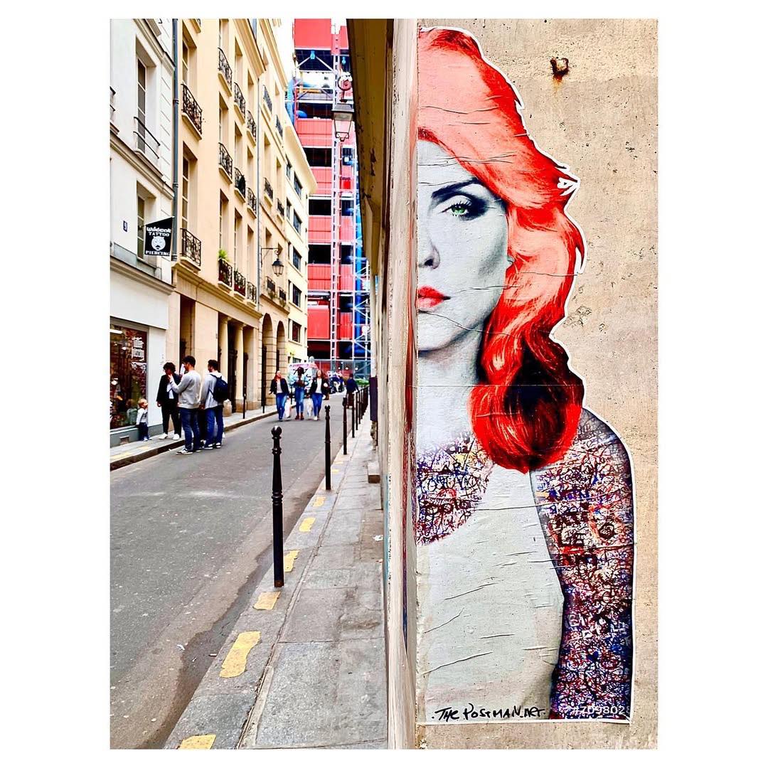 Large street art portrait of Debbie Harry with red hair on a Paris building wall, pedestrians on sidewalk