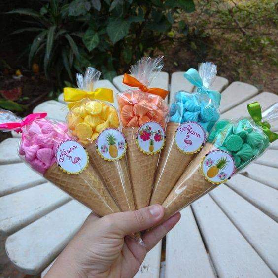 Hand holding colorful candy-filled paper cone party favors with ribbons on a white outdoor table