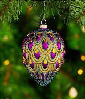 Decorative teardrop Christmas ornament with teal, gold, and purple peacock pattern on a pine tree