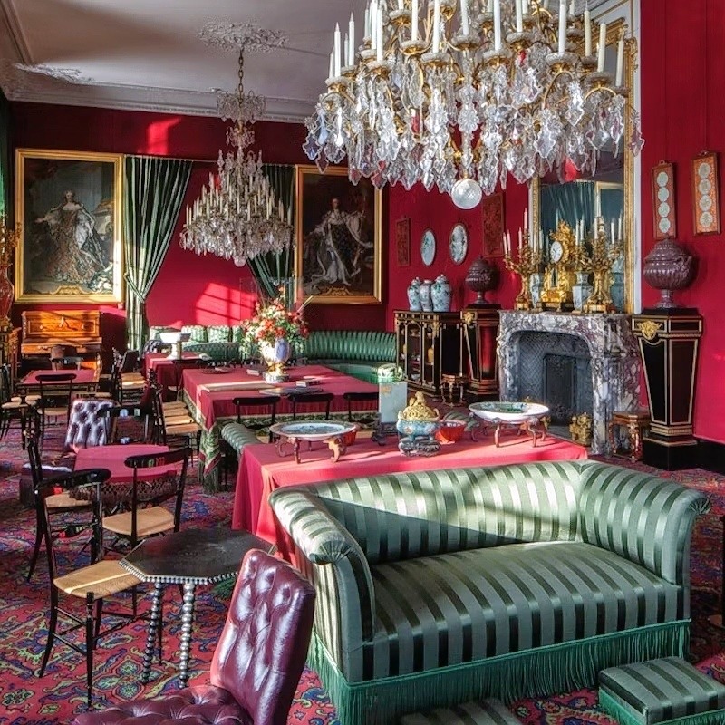 Luxurious palace room with crystal chandeliers, red walls, striped sofas, paintings, and ornate golden decorations