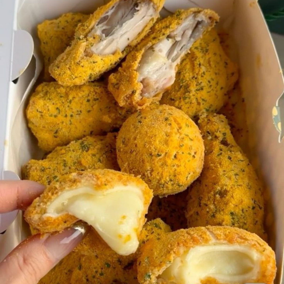 Golden fried Korean street snacks in a box, with one piece showing melted cheese inside
