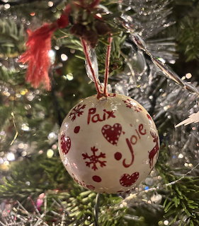 White Christmas ornament with red designs hanging on a tree with silver tinsel