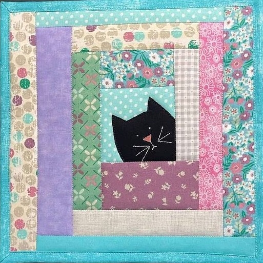 Black cat silhouette peeking from colorful patchwork quilt square with floral and geometric patterns