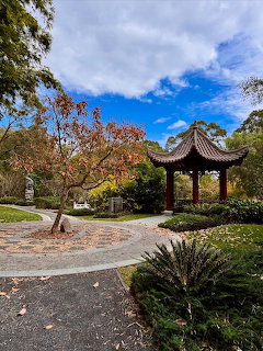 Traditional Chinese pavilion with dark curved roof in a garden setting with trees and blue sky