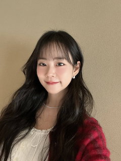 Young Asian woman with long dark hair and bangs smiling in a red plaid cardigan and white top