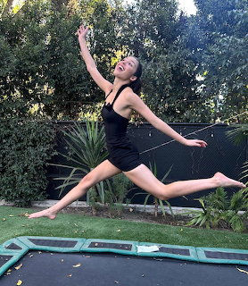 Woman mid-air jumping on trampoline in garden with arms outstretched