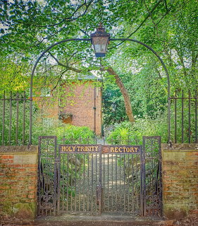 Iron gate entrance to Holy Trinity Church rectory surrounded by green foliage and brick walls