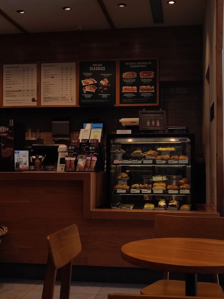 Cozy cafe interior with glass pastry display case, menu boards on wall, and wooden tables and chairs