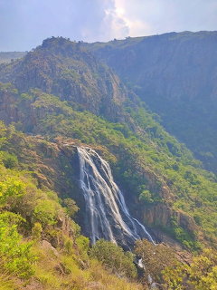 Waterfall flowing down verdant mountain with cloudy sky in Eswatini national park