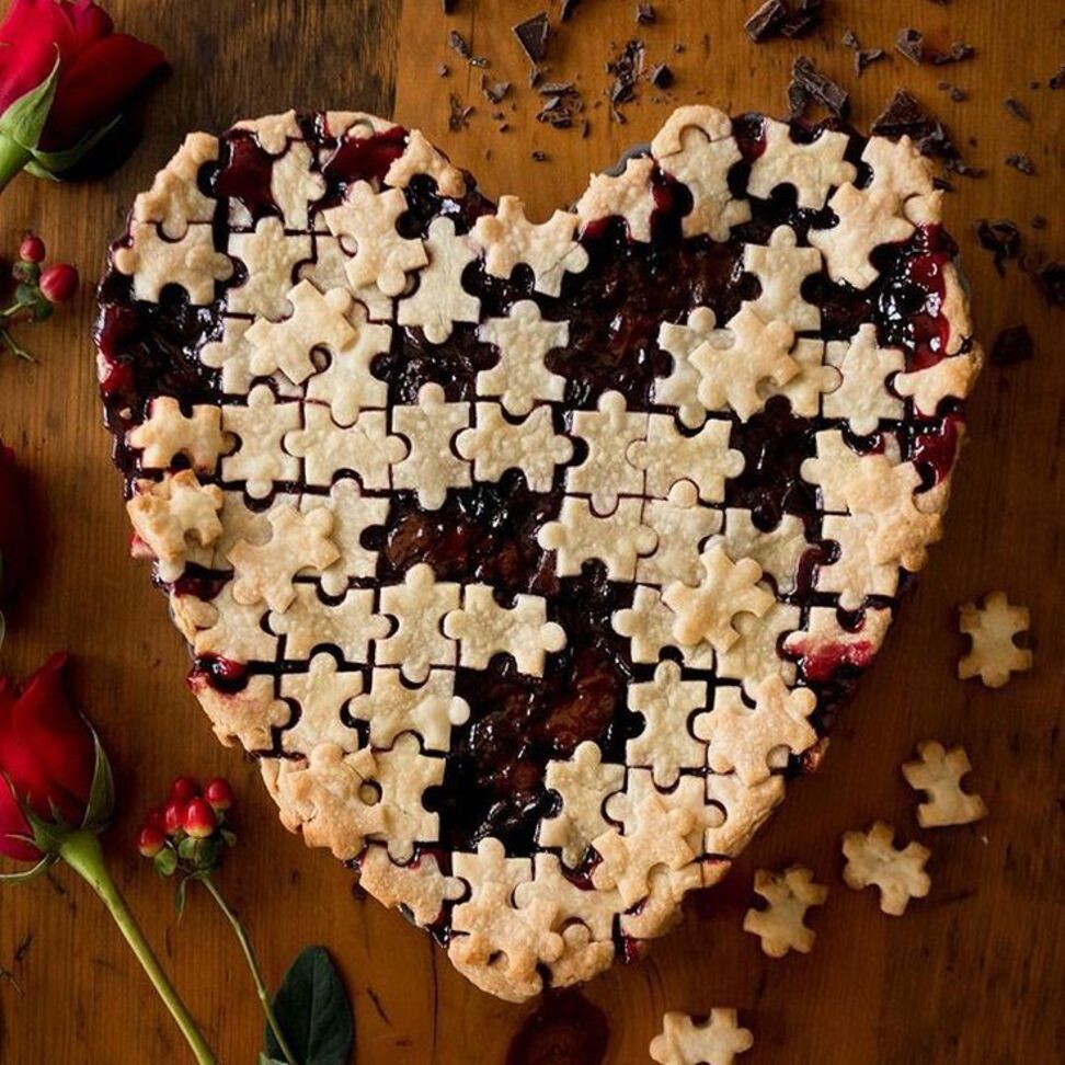 Heart-shaped berry pie styled as a jigsaw puzzle on a wooden table with red roses