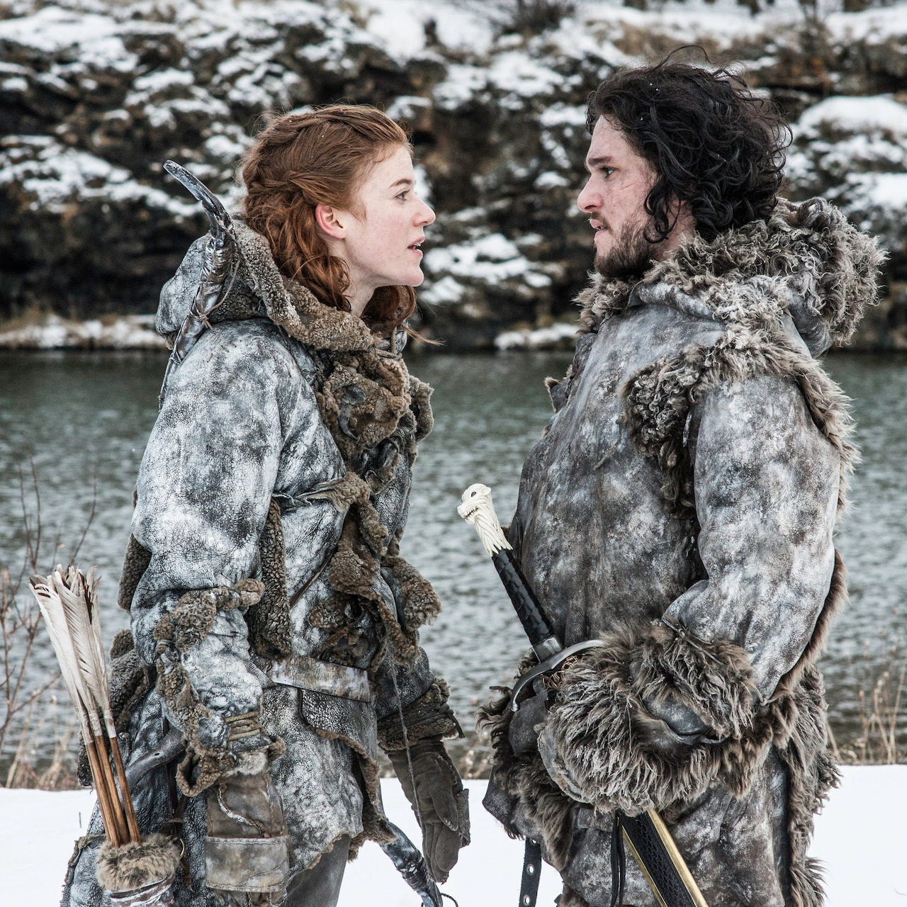 Two people in fur clothing standing by a snowy river