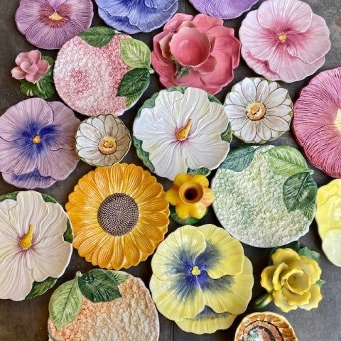 Assorted ceramic flower-shaped decorative plates in pastel and bright colors arranged on a dark background