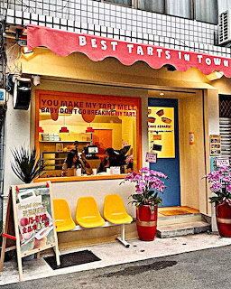 Vibrant pink and yellow bakery storefront with awning reading 'Best Tarts in Town' and outdoor seating