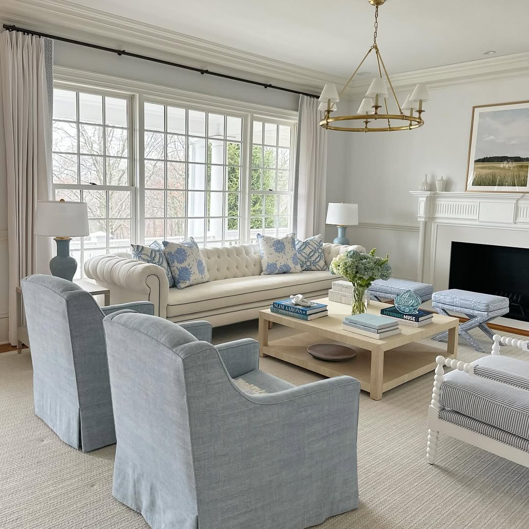 Bright coastal living room with blue-gray chairs, sofa, large windows, and white fireplace