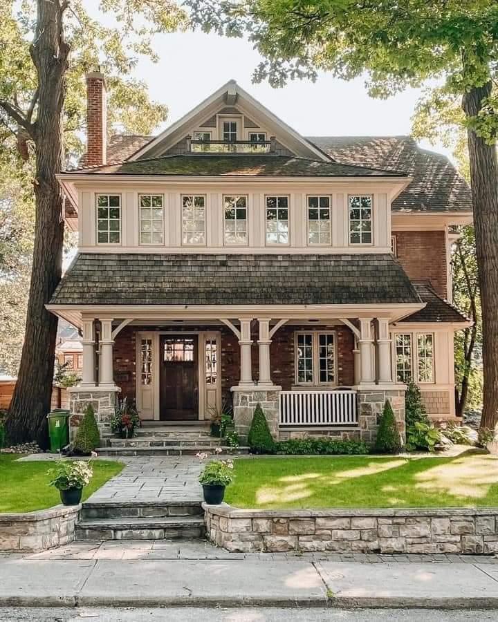 Two-story Craftsman house with gray siding, pink shutters, covered porch, and green lawn with trees