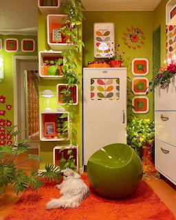 Retro 1970s room with green walls, orange carpet, colorful shelves, plants, white fridge, and green ball chair