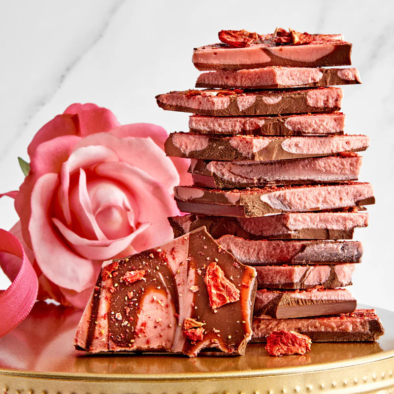 Stacked strawberry chocolate bark pieces with pink rose decoration on marble surface