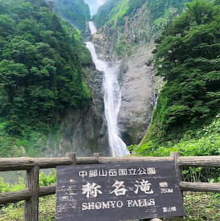 Tall waterfall flowing down mountain gorge with dense green vegetation and viewing platform with wooden sign in foreground