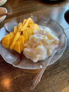 Glass plate with sliced yellow mango and sticky rice with coconut milk on wooden table