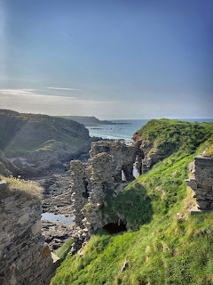 Stone ruins of Findlater Castle on steep grassy cliff overlooking the Scottish coastline and blue sea