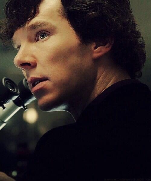 Close-up of a man with dark curly hair aiming a rifle in dim cinematic lighting
