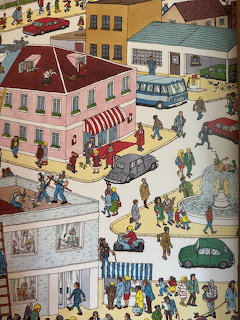 Detailed cartoon illustration of a busy town street with buildings, cars, buses, and many people