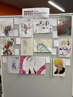 Display board with multiple hand-drawn manga and anime character artworks pinned up for Manga Day 24 event