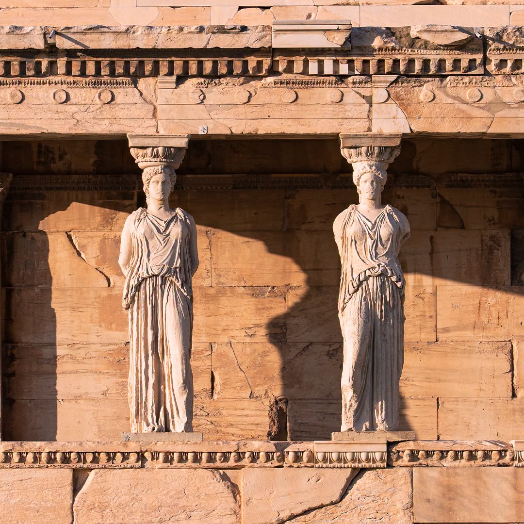 Two caryatid statues supporting an ancient Greek stone temple facade