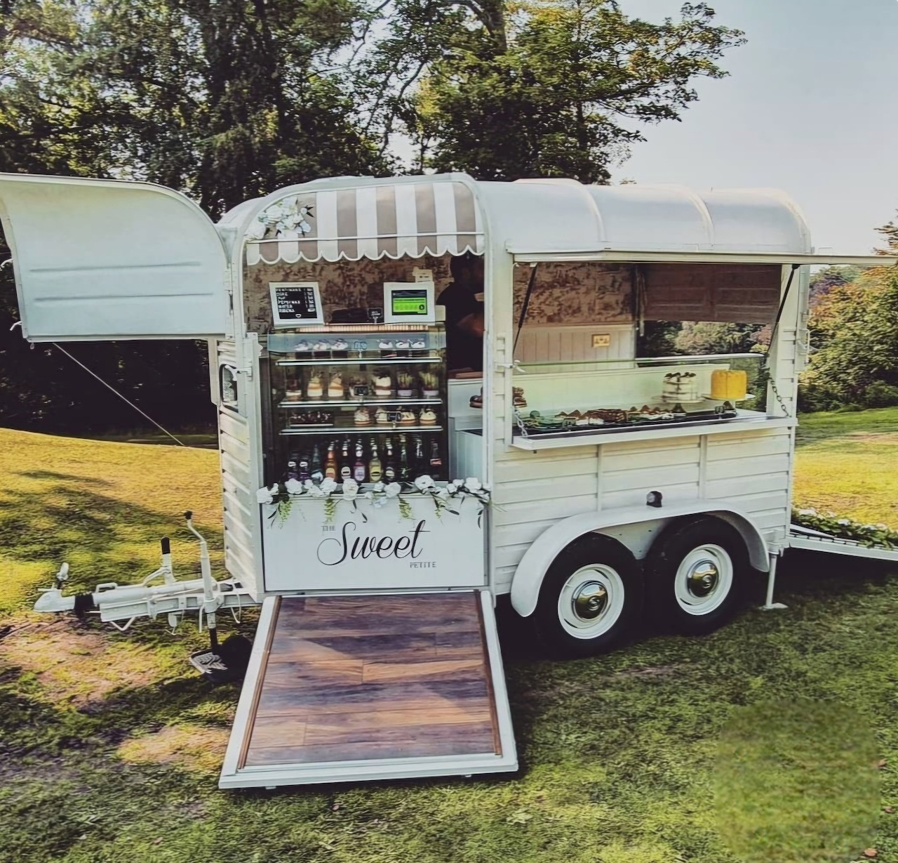 Vintage coffee trailer on grass with open counter, shelves, and a ramp