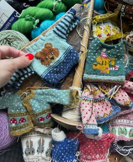 Colorful miniature knitted sweaters, yarn, and craft supplies on a rustic tabletop