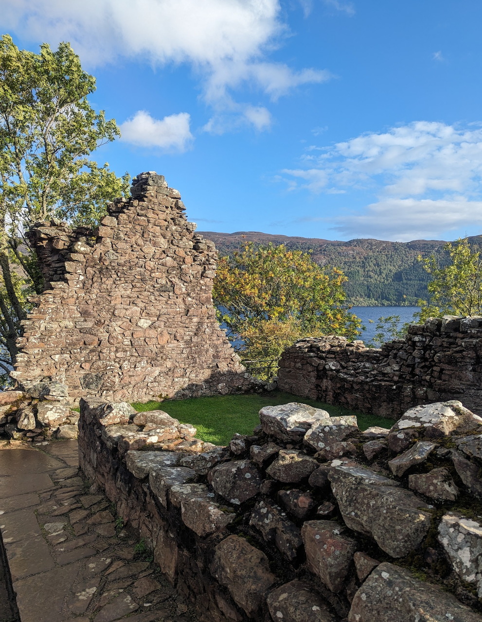 Stone ruins of Urquhart Castle with loch and green hills under blue sky