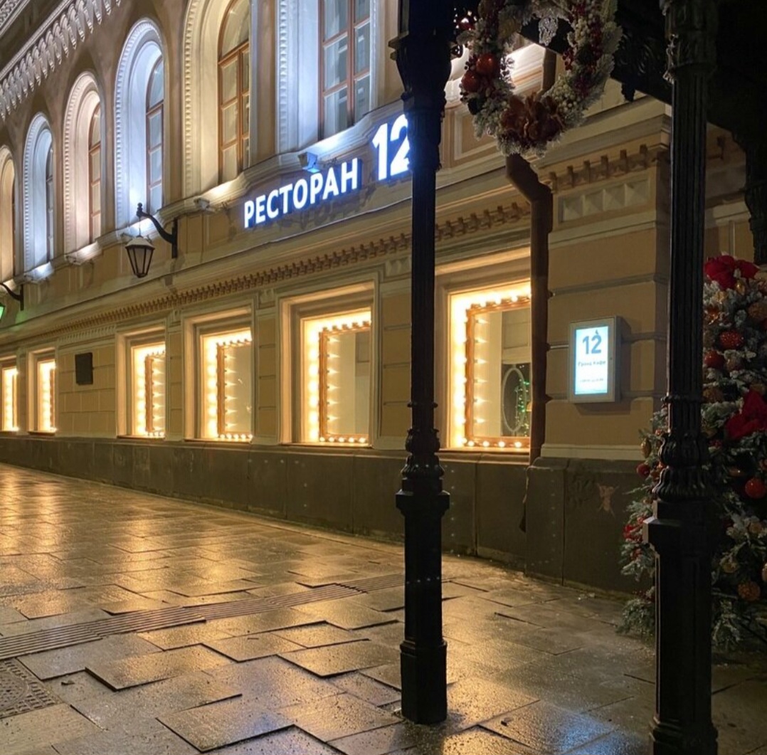 Night view of elegant lit restaurant building with arched windows and ornate architectural details on empty plaza