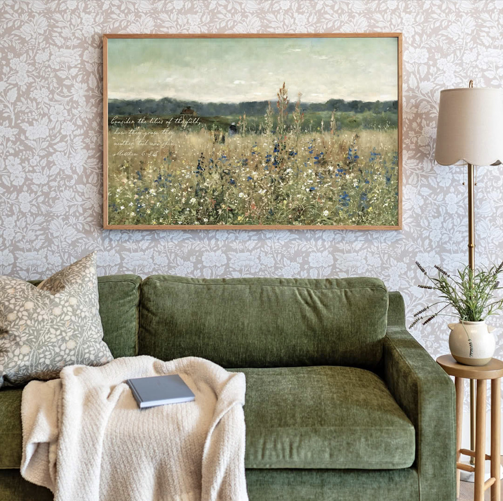 Cozy living room with green sofa, framed landscape painting, floor lamp, and plant on a side table