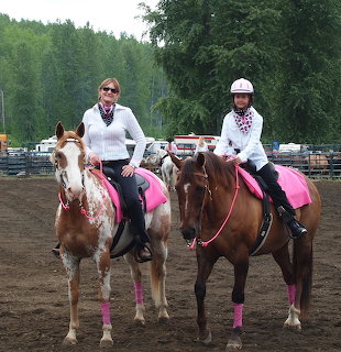 Two riders on brown horses with pink tack in an outdoor riding arena