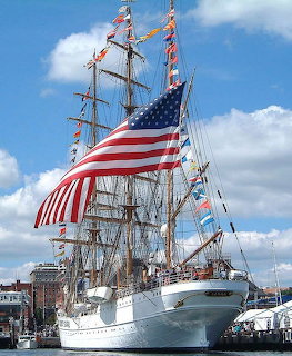 White tall ship USCGC Eagle with masts and American flag at dock under blue sky