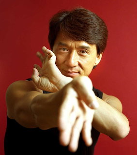 Jackie Chan posing with fists extended toward camera against a red background