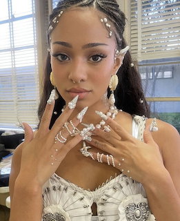 Portrait of a woman in white ornate top with braided hairstyle and jewelry posing indoors