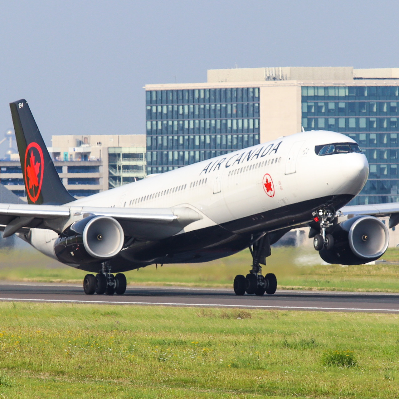 Air Canada Airbus A330 aircraft on runway with red maple leaf livery, airport buildings behind