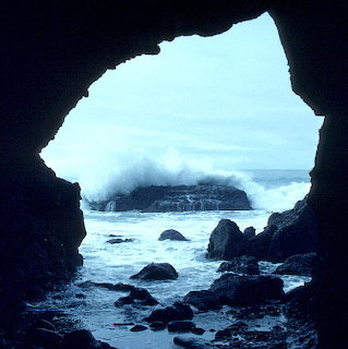 Ocean view through dark sea cave opening with rocks and misty coastline
