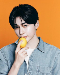 Studio portrait of Hanbin in a denim shirt holding a yellow fruit against an orange background.