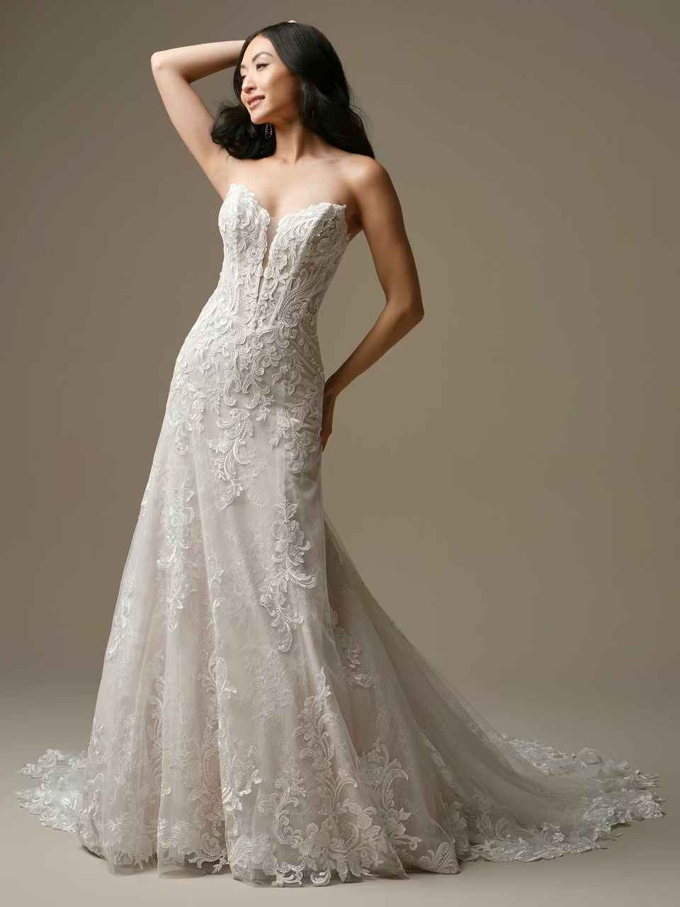 Bride in strapless white lace wedding gown with train on neutral background