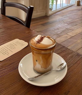 Glass of Viennese-style coffee with whipped cream on a white saucer on a wooden table